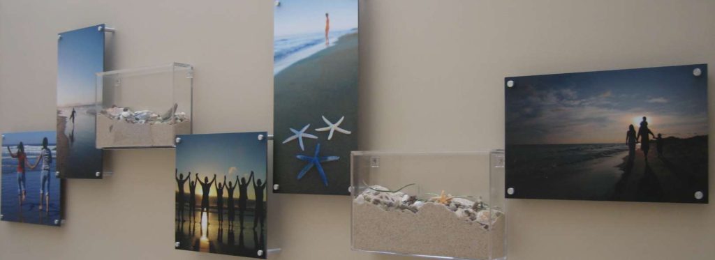 Example of biophilic artwork in healthcare. Collage of printed beach images with clear acrylic boxes filled with sand and seashells.